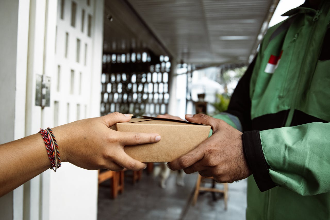 A delivery person hands over a package to a recipient in a close-up view outdoors.